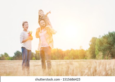 Happy Family Walking In Wheat Field With Yellow Lens Flare In Background