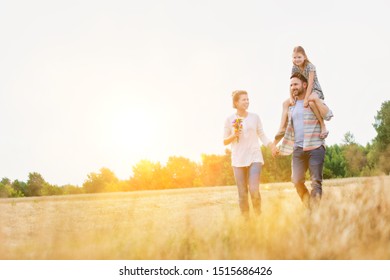 Happy Family Walking In Wheat Field With Yellow Lens Flare In Background