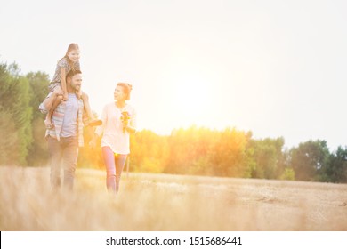 Happy Family Walking In Wheat Field With Yellow Lens Flare In Background