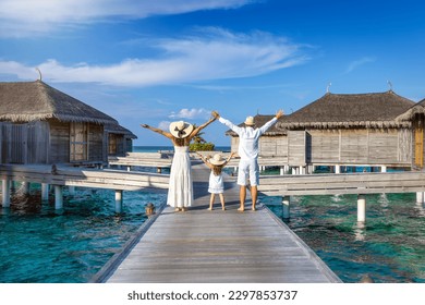 A happy family walks over a wooden pier between over water lodges in the Maldives islands during their tropical vacations - Powered by Shutterstock