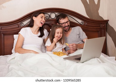 Happy Family Watching Movie In Bed And Eating Chips.