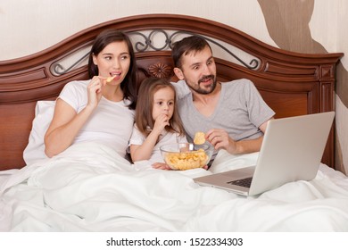 Happy Family Watching Movie In Bed And Eating Chips.