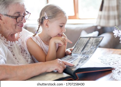 Happy Family Watching Old Photo Album At Home Together. Senior Woman Showing Child Black And White Vintage Photos. Retired Person Memories. Leisure Of Grandmother And Kid. Lifestyle Authentic Moment.