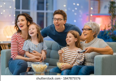 Happy family watching projector, TV, movies with popcorn in the evening at home. Granny, mother, father and daughters spending time together.