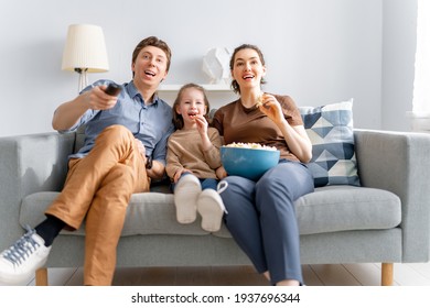 Happy family watching projector, TV, movies with popcorn in the evening at home. Mother, father and daughter spending time together.