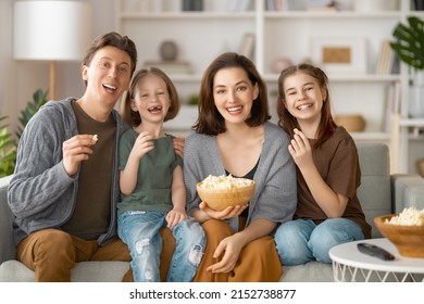 Happy family watching projector, TV, movies with popcorn in the evening at home. Mother, father and daughters spending time together.