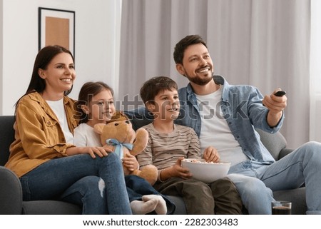 Happy family watching TV at home. Father changing channels with remote control