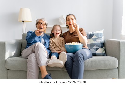 Happy family watching TV, movies with popcorn at home. Mother, daughter and grandmother spending time together.