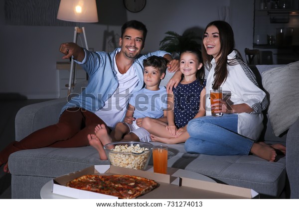 Happy family watching\
TV on sofa at night