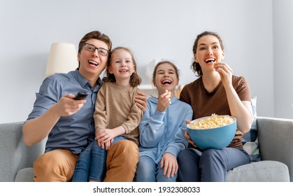 Happy family watching TV with popcorn  at home. Mother, father and daughters spending time together.