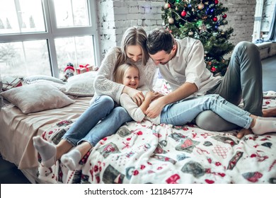 Happy Family Wearing Lying On Bed. Mother Father And Child Having Fun In Christmas Time. Man, Woman And Kid Relaxing At Home. Winter Holiday Xmas And New Year Concept