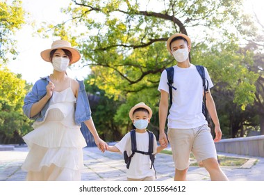 Happy Family Wearing The Medical Mask And Walking In The Park. Family Vacations During Coronavirus Covid-19 Pandemic.