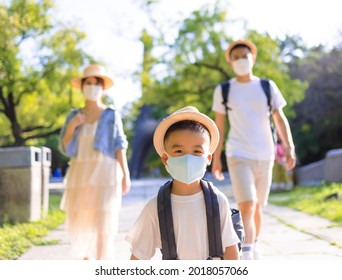 Happy Family Wearing The Medical Mask And Walking In The Park. Family Vacations During Coronavirus Covid-19 Pandemic.