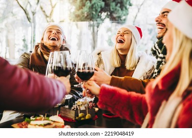 Happy family wearing santa claus hat having Christmas dinner party- Cheerful group of friends sitting at restaurant dining table celebrate xmas holiday cheering red wine glasses together
