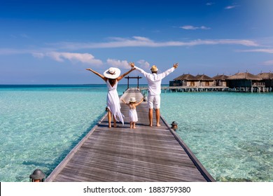 A happy family in white summer clothing on vacation walks along a wooden pier over tropical, turquoise ocean in the Maldives, Indian Ocean - Shutterstock ID 1883759380