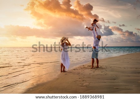 A happy family in white summer clothing is having fun on a tropical beach during sunset time