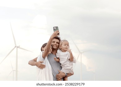 Happy family at wind turbine farm. Mother and father who carry daughter take selfie together with smartphone at sunset sky windmill park. Parents and girl kid, ecology alternative renewable energy. - Powered by Shutterstock