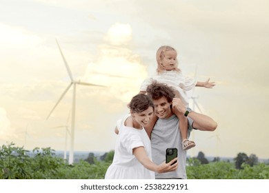 Happy family at wind turbine farm. Mother and father who carry daughter take selfie together with smartphone at sunset sky windmill park. Parents and girl kid, ecology alternative renewable energy. - Powered by Shutterstock