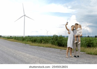 Happy family at wind turbine farm. Father, mother and daughter spend time together at cloudy sky windmill park. Parents and girl kid take selfie with smartphone. Ecology alternative renewable energy. - Powered by Shutterstock