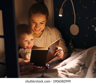 Happy Family Woman And Boy Cuddling And Smiling While Reading Book On Bed Near Lamp At Night At Home