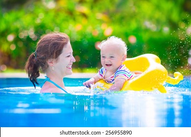 Happy Family, Young Active Mother And Adorable Curly Little Baby Having Fun In A Swimming Pool, Child Learning To Swim In An Inflatable Toy Ring, Enjoying Summer Vacation At A Tropical Resort