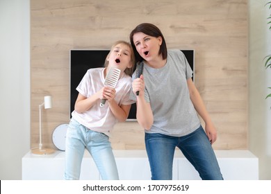 Happy Family Young Adult Mother And Cute Teen Daughter Having Fun Singing Karaoke Song In Hairbrushes. Mother Laughing Enjoying Funny Lifestyle Activity With Teenage Girl At Home Together.