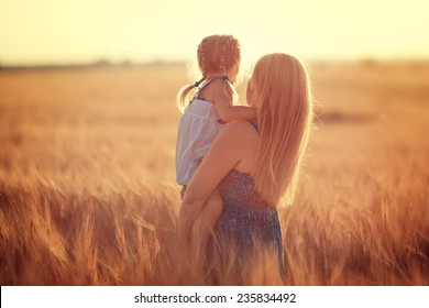 Happy family: a young beautiful pregnant woman with her little cute daughter walking in the wheat orange field on a sunny summer day. Parents and kids relationship. Nature in the country.