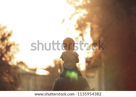 Happy family: Young father with his little child sitting on father's shoulders in Summer in City at Beautiful Sunset  
