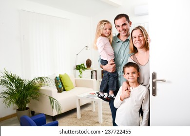 Happy Family With Young Kids Welcoming A Guests At Their House Door Wide Open.