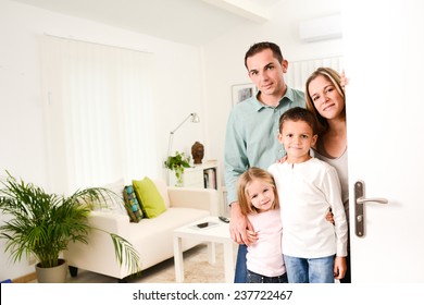 Happy Family With Young Kids Welcoming A Guests At Their House Door Wide Open.