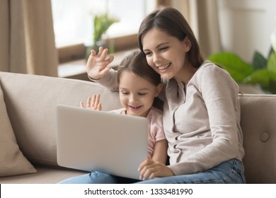 Happy Family Young Mom With Kid Daughter Looking At Laptop Screen Waving Hands Make Distance Video Call, Smiling Mother And Little Child Girl Talking To Webcamera On Internet Chat By Computer Webcam