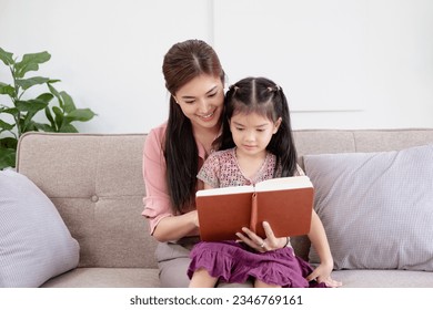 Happy family young mother babysitter hold read book relax embrace cute little children daughters, smiling parent mum tell small kids funny fairy tale story sit on sofa having fun together at home - Powered by Shutterstock