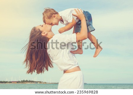 Happy family. Young mother throws up baby in the sky, on sunny day. Portrait mom and little son on the beach. Positive human emotions, feelings, joy.