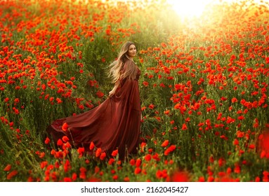 Happy fantasy woman queen in red silk dress, walking in poppy field, summer green grass, nature flowers. Girl goddess princess train hem skirt flying in wind satin fabric waving. art divine sun light
