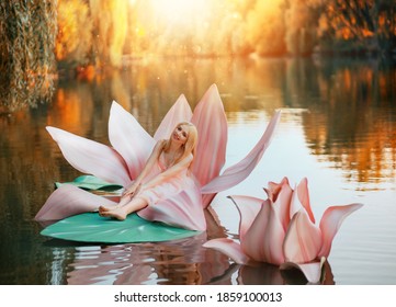 Happy Fantasy Young Blonde Woman Little Fairy Princess Sitting In Pink Lotus Flower On Lake Water. Elf Girl, With Smiling Face. Autumn Nature Background Orange Trees Divine Magic Sun Light. Pink Dress