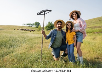 Happy Farm Family Looking At Camera Near Herd Grazing In Scenic Meadow