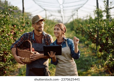 Happy farm workers using digital tablet while harvesting apples in orchard. - Powered by Shutterstock