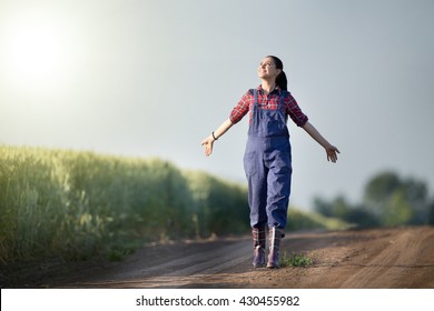 Happy farmer girl walking beside green wheat field with stretched arms and enjoying the sun