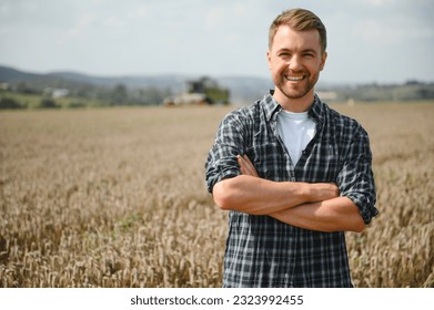 Happy farmer proudly standing in a field. Combine harvester driver going to crop rich wheat harvest. Agronomist wearing flannel shirt, looking at camera on a farmland. - Shutterstock ID 2323992455