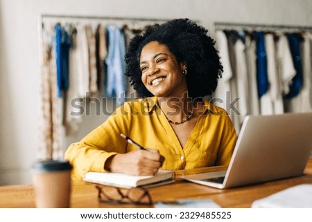 Happy fashion designer smiling confidently as she writes down plans for her small business in a note book. Creative young woman using her entrepreneurial ideas in running a clothing store.