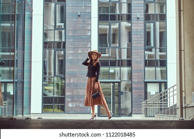 Happy fashion elegant woman wearing a black jacket, brown hat and skirt with a handbag clutch walking on the European city center. - Shutterstock ID 1122018485