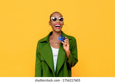Happy fashionable African American woman smiling and showing credit card in hand on yellow isolated background for cashless society concept