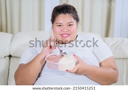 Happy fat woman eating ice cream while sitting on the couch. Shot at home