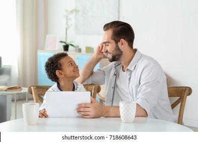 Happy father with adopted African-American boy using tablet computer in living room - Powered by Shutterstock