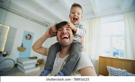 Happy father carrying his smiling son on neck and making selfie on smartphone in bedroom