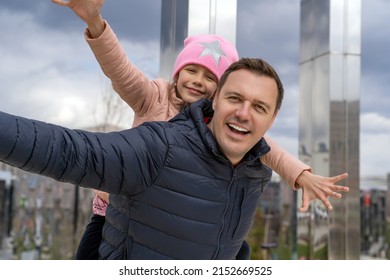 Happy Father Carrying Piggyback Ride To His Daughter Outdoors. Cheerful Girl Piggyback Riding Dad In Park, Spending Time Together