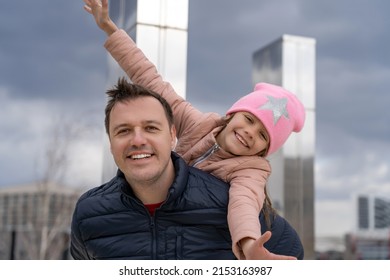 Happy Father Carrying Piggyback Ride To His Daughter Outdoors. Cheerful Girl Piggyback Riding Dad In Park, Spending Time Together