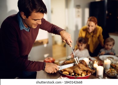 Happy Father Carving Thanksgiving Turkey During A Meal With His Family At Dining Table. 