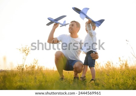 Happy father child moment. Father piggybacking his boy at sunset while he's playing with toy plane