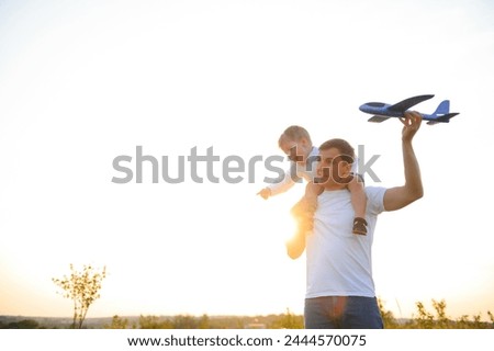 Happy father child moment. Father piggybacking his boy at sunset while he's playing with toy plane
